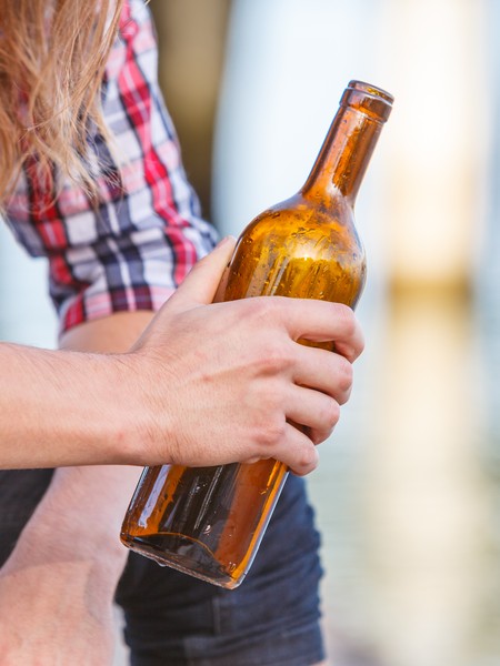 Ein junger Mann hält eine Bierflasche in der Hand. Im Detail sieht man Hand und Bierflasche.